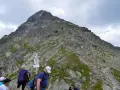 Grupa turystów na szlaku w Tatrach, w tle skalisty szczyt i tabliczka wskazująca świnicka przełęcz.