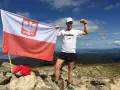 Mężczyzna z polską flagą na szczycie górskim, zdobywca diadem polskich gór, dumny z osiągnięcia.