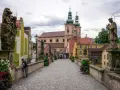 Kamienna, brukowana ścieżka prowadzi do barokowego kościoła z zielonymi wieżami. Wzdłuż mostu stoją kamienne rzeźby. To piękne ziemia kłodzka atrakcje.