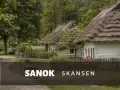 Skansen Sanok: tradycyjne chaty kryte strzechą, zielone drzewa i płot. Sprawdź cennik i zaplanuj wizytę!