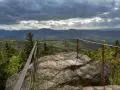 Widok z punktu widokowego na **przełęczy lądeckiej**. Skaliste podłoże, metalowa balustrada i rozległy, zalesiony krajobraz pod burzowym niebem.
