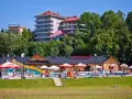 Słoneczny dzień w Muszynie-Zdroju. Ludzie relaksują się przy basenie zjeżdżalnią, a w tle widać hotel i restaurację.