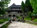 Kamienny budynek schroniska w Dolinie Chochołowskiej z ludźmi na schodach i rowerzystą na kamiennej drodze.