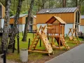 Drewniany plac zabaw z domkami w tle. Idealne bory tucholskie atrakcje dla dzieci, gdzie można odpocząć i bawić się na świeżym powietrzu.