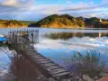 Spokojny zalew czorsztyński z pomostem i łódkami, w tle zalesione wzgórza i zamek.