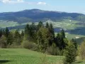 Widok na górzysty krajobraz z lasami, łąkami i wioską w dolinie.