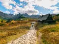 Kamienista ścieżka prowadzi do Rusinowej Polany, gdzie widać drewniane chaty i turystów. W tle majestatyczne Tatry.