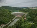 Widok z lotu ptaka na zalesione wzgórza i dużą kamienną zaporę wodną z budynkami.