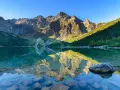 Spokojne jezioro odbija skaliste szczyty. Woda jest krystalicznie czysta, widać kamienie na dnie. To właśnie tutaj, gdzie są Tatry, natura zachwyca.