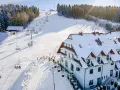 Hotel ze stokiem narciarskim dla dzieci. Kolejka krzesełkowa wwozi narciarzy na ośnieżony stok, a obok hotelu bawią się dzieci.