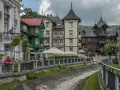 Krynica-Zdrój latem: malownicza promenada nad potokiem, zabytkowe wille i kawiarniane ogródki.