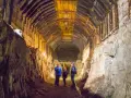 Zwiedzanie podziemnego kompleksu Projekt Riese. Trzech turystów w kaskach oświetla latarkami mroczny tunel z drewnianymi stropami.