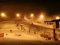 Oświetlony stok narciarski Gołębiewski nocą, z armatkami śnieżnymi i narciarzami.