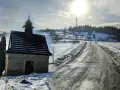 Kamienna kapliczka na zboczu Koskowej Góry, zimowa droga i słońce.