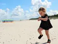 Radosna dziewczynka biega po piaszczystej plaży. Wspaniałe wakacje na Słowacji z dziećmi to marzenie każdego rodzica.