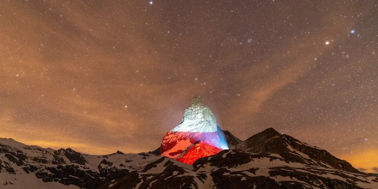 Górski szczyt, niczym polski Matterhorn, rozświetlony nocą polskimi barwami pod rozgwieżdżonym niebem.