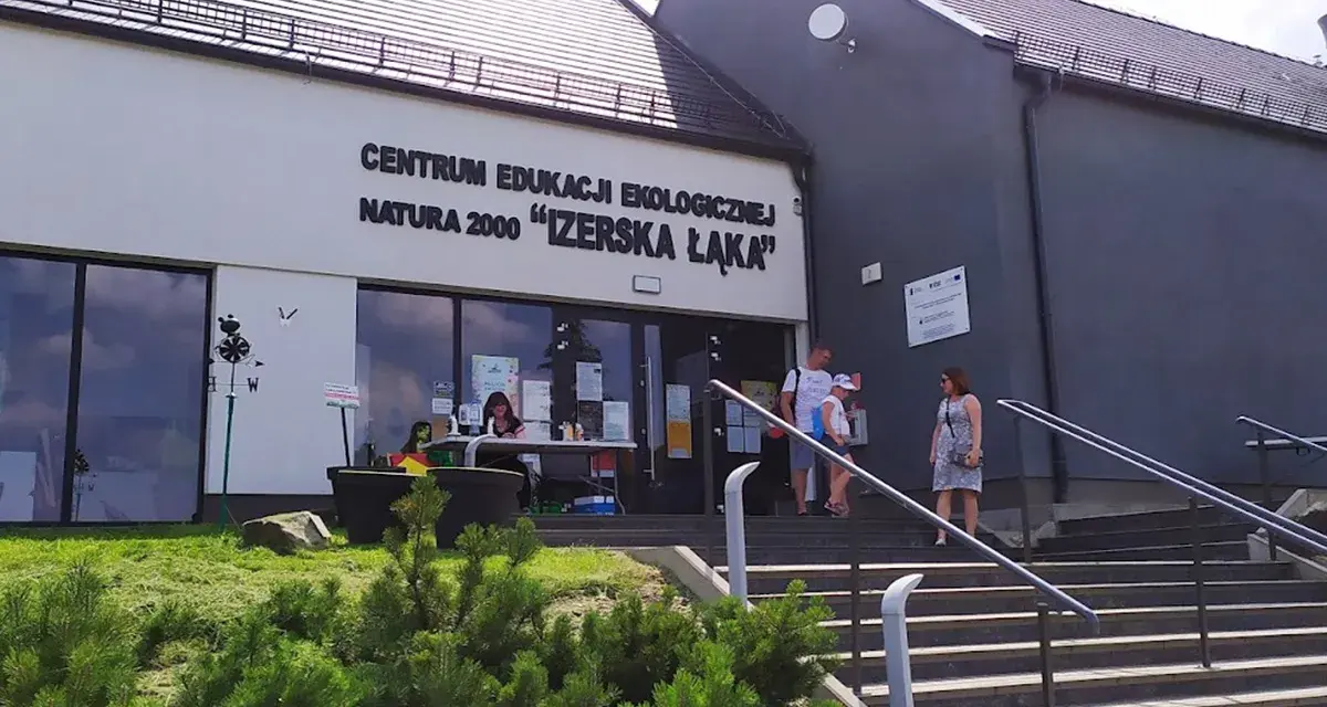 Centrum Edukacji Ekologicznej Natura 2000 "Izerska Łąka" zaprasza. Rodzina wchodzi po schodach do budynku.