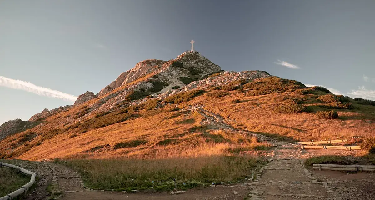 Giewont, szczyt widoczny z Krupówek, w złotym świetle zachodzącego słońca. Kamienista ścieżka prowadzi ku górze.