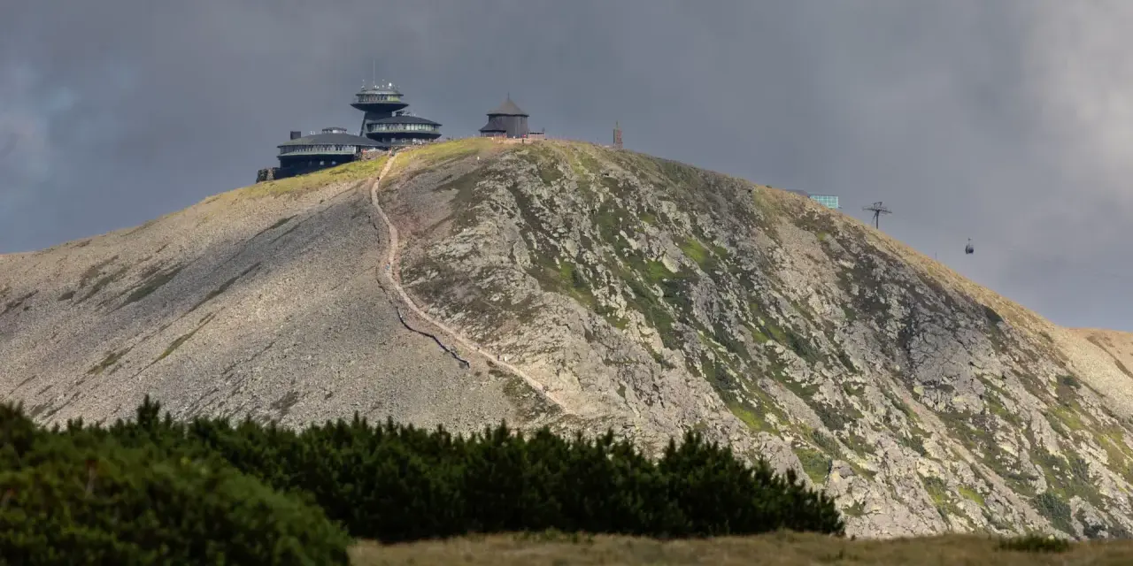 Schronisko i obserwatorium na szczycie w Karkonoszach, z widoczną kolejką linową i kamienistym zboczem.