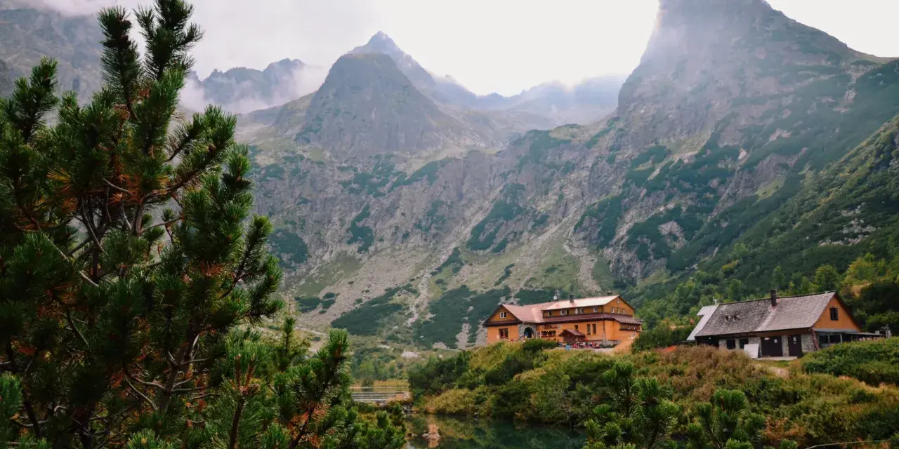 Słowackie Tatry: schroniska nad jeziorem, otoczone zielenią i majestatycznymi szczytami, z mgłą unoszącą się w tle.