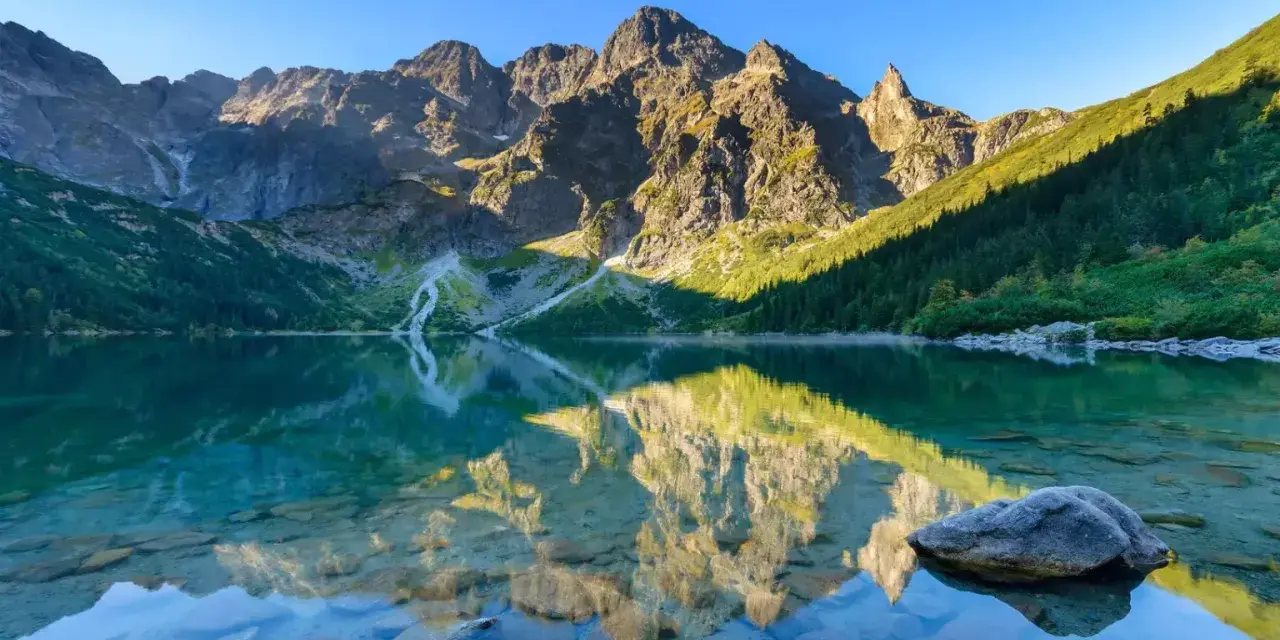 Spokojne jezioro odbija skaliste szczyty. Woda jest krystalicznie czysta, widać kamienie na dnie. To właśnie tutaj, gdzie są Tatry, natura zachwyca.