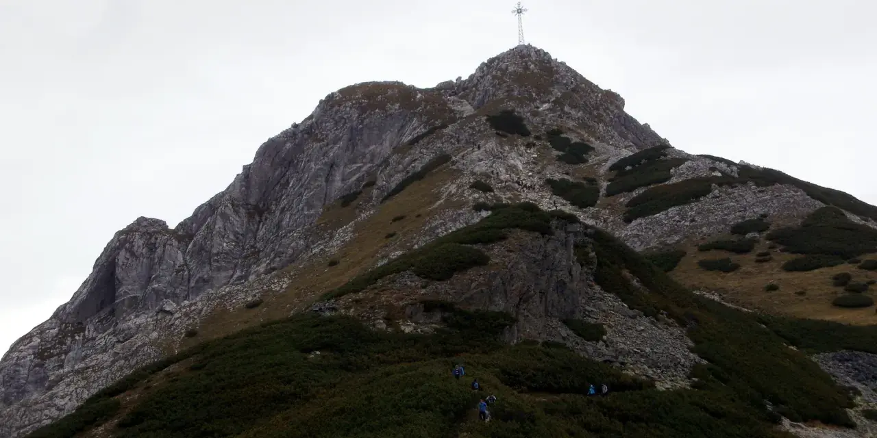 Grupa turystów podąża szlakiem na Giewont. W oddali widać charakterystyczny krzyż na szczycie.