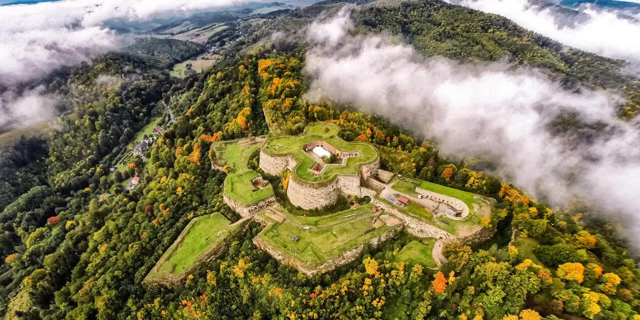 Twierdza na wzgórzu, otoczona jesiennym lasem, to jedna z głównych atrakcji Srebrnej Góry. Mgła spowija okoliczne góry.