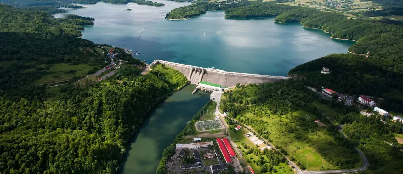 Zapora Solina z lotu ptaka, otoczona zielonymi wzgórzami i błękitną wodą. Planujesz wycieczkę? Sprawdź zapora Solina bilety!