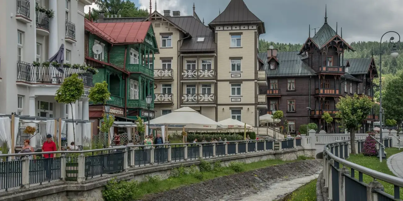 Krynica-Zdrój latem: malownicza promenada nad potokiem, zabytkowe wille i kawiarniane ogródki.
