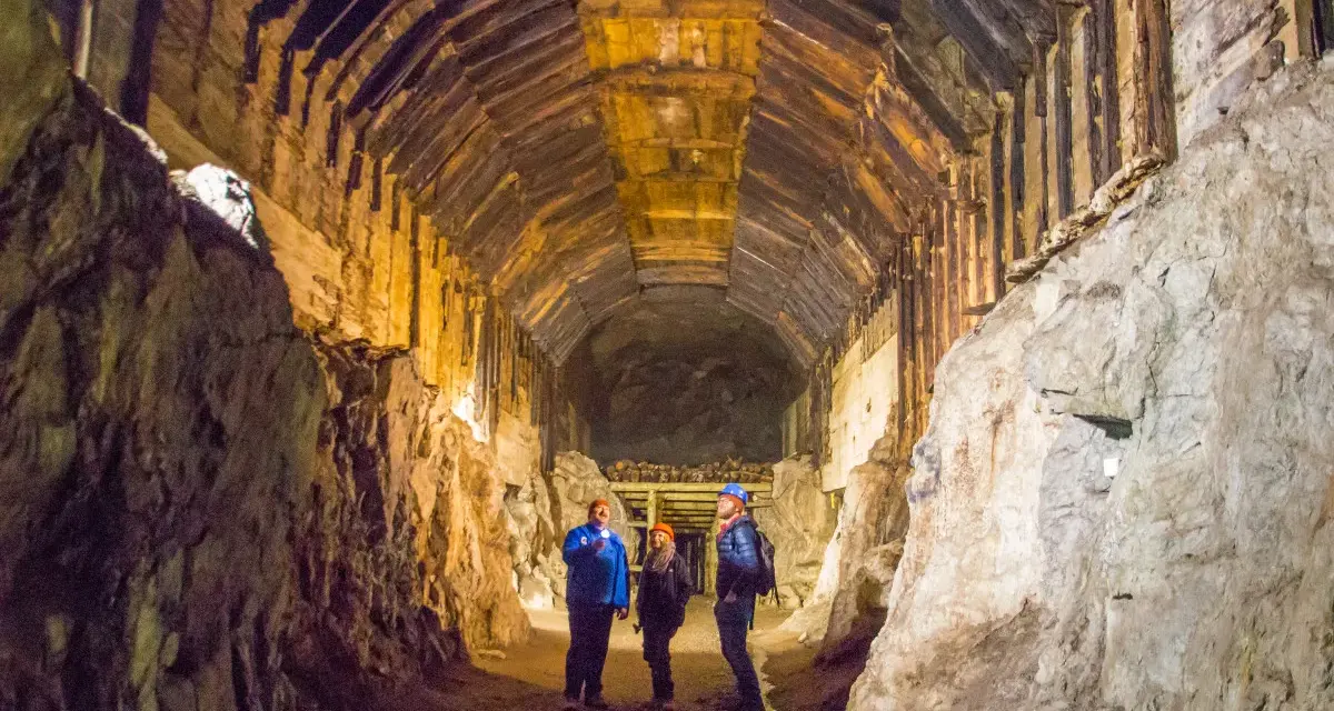 Zwiedzanie podziemnego kompleksu Projekt Riese. Trzech turystów w kaskach oświetla latarkami mroczny tunel z drewnianymi stropami.