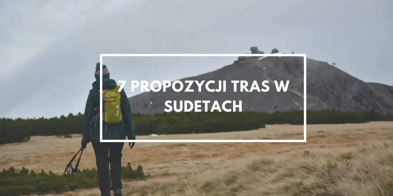 Turystka z plecakiem i kijkami maszeruje przez trawiaste tereny w Sudetach, zmierzając ku górze z budynkami.