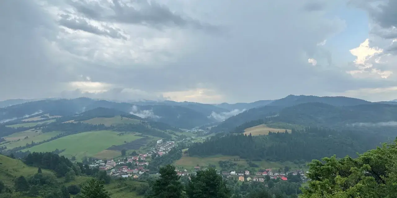 Widok na dolinę z wioską i wzgórzami w tle, chmury nad przełęczą pod Tokarnią.