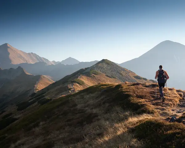Wędrowiec na grani Tatr, odkrywa malownicze tatry szlaki dla średnio zaawansowanych. Słońce oświetla zbocza.