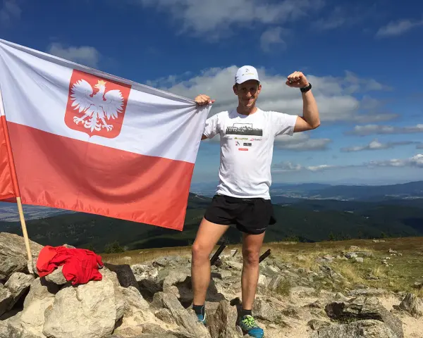Mężczyzna z polską flagą na szczycie górskim, zdobywca diadem polskich gór, dumny z osiągnięcia.