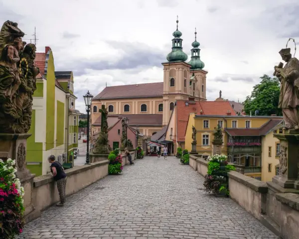 Kamienna, brukowana ścieżka prowadzi do barokowego kościoła z zielonymi wieżami. Wzdłuż mostu stoją kamienne rzeźby. To piękne ziemia kłodzka atrakcje.