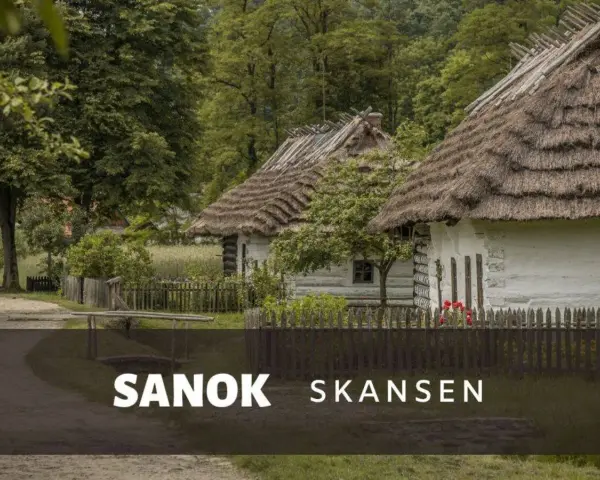 Skansen Sanok: tradycyjne chaty kryte strzechą, zielone drzewa i płot. Sprawdź cennik i zaplanuj wizytę!