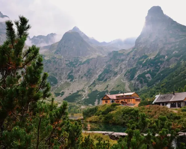 Słowackie Tatry: schroniska nad jeziorem, otoczone zielenią i majestatycznymi szczytami, z mgłą unoszącą się w tle.