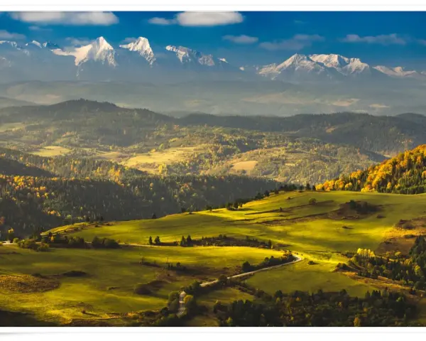 Widok na Tatry z ośnieżonymi szczytami, w tym Trzy Korony. Jesienne wzgórza pokryte złotymi liśćmi i zielonymi łąkami.
