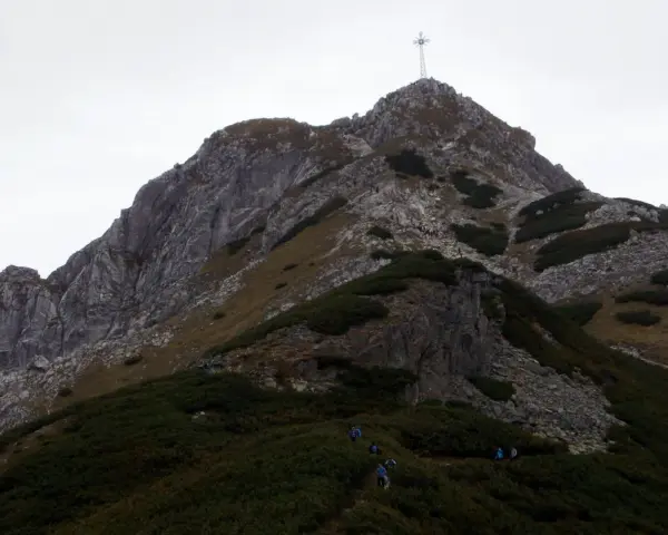Grupa turystów podąża szlakiem na Giewont. W oddali widać charakterystyczny krzyż na szczycie.