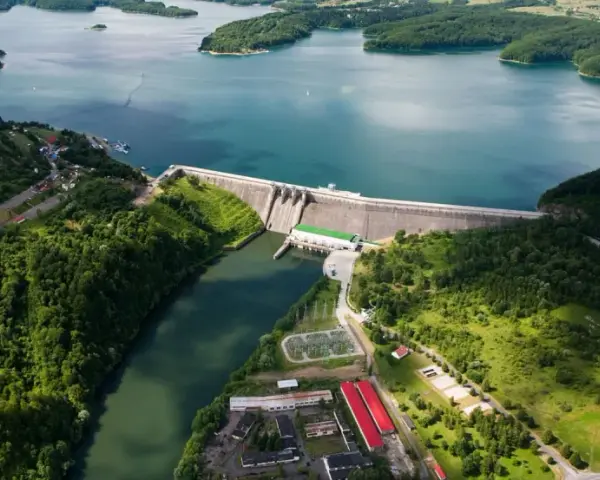 Zapora Solina z lotu ptaka, otoczona zielonymi wzgórzami i błękitną wodą. Planujesz wycieczkę? Sprawdź zapora Solina bilety!