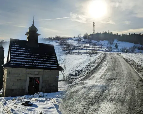 Kamienna kapliczka na zboczu Koskowej Góry, zimowa droga i słońce.