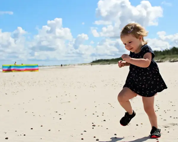 Radosna dziewczynka biega po piaszczystej plaży. Wspaniałe wakacje na Słowacji z dziećmi to marzenie każdego rodzica.