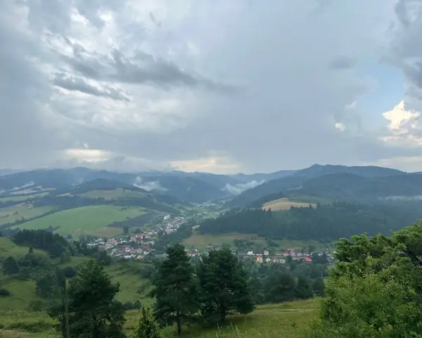 Widok na dolinę z wioską i wzgórzami w tle, chmury nad przełęczą pod Tokarnią.
