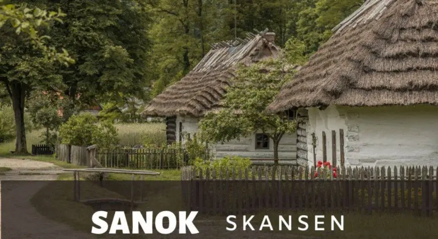 Skansen Sanok: tradycyjne chaty kryte strzechą, zielone drzewa i płot. Sprawdź cennik i zaplanuj wizytę!
