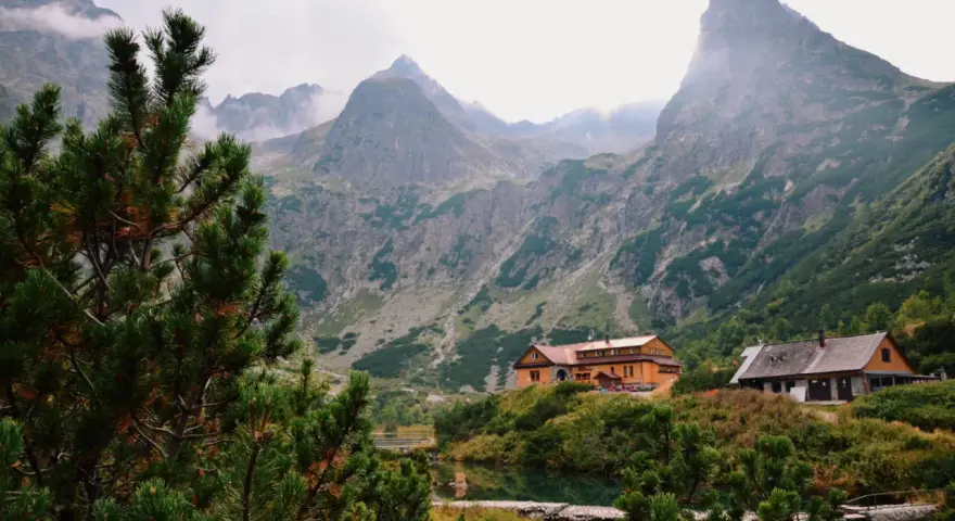 Słowackie Tatry: schroniska nad jeziorem, otoczone zielenią i majestatycznymi szczytami, z mgłą unoszącą się w tle.