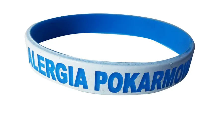 Niebieska opaska na ręce z napisem "ALERGIA POKARMOWA" informuje o problemach z jedzeniem.