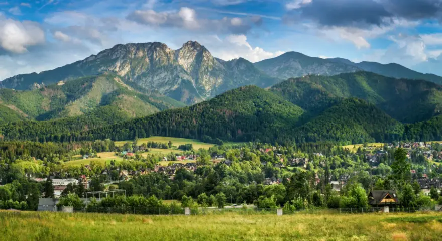 Malowniczy widok na Tatry z Jaszczurówki, gdzie liczne atrakcje czekają na turystów. Zielone wzgórza i tradycyjna zabudowa tworzą sielski krajobraz.