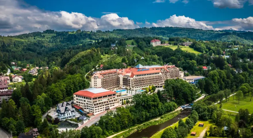 Hotel Gołębiewski w otoczeniu zielonych wzgórz i rzeki.