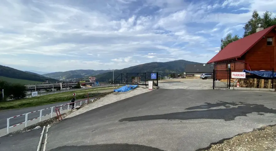 Widok na parking przy górze Żar. W oddali widać zabudowania i góry.