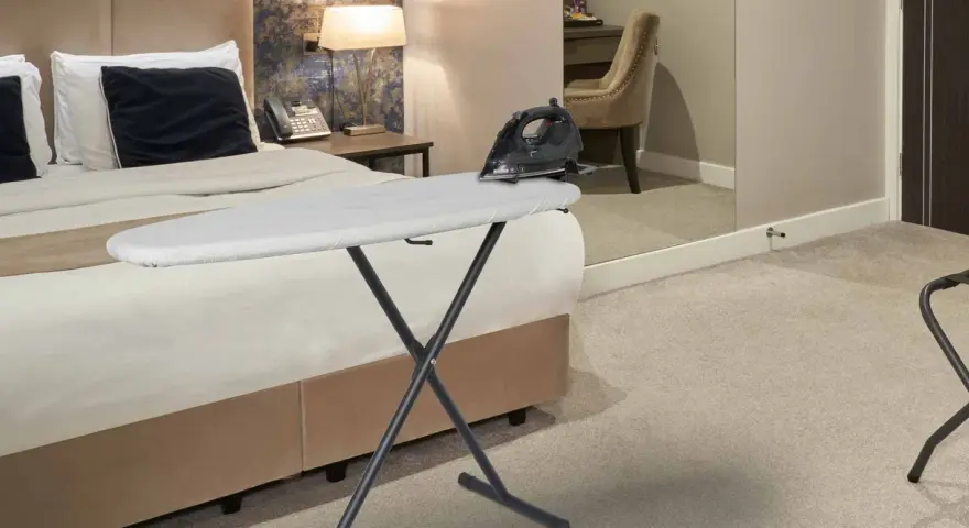 Deska do prasowania z żelazkiem na łóżku w hotelowym pokoju.